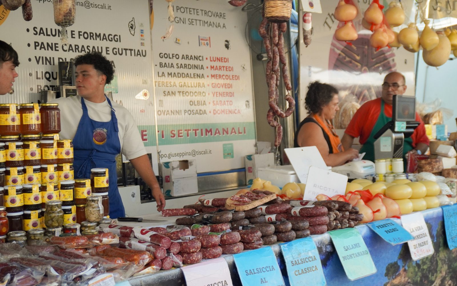 La famiglia al lavoro dietro al banco del mercato, fra salumi, formaggi e conserve